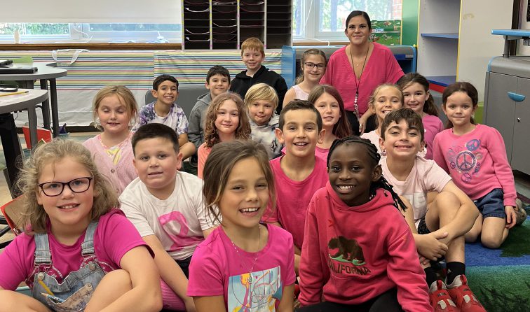 bunch of elementary students sitting on the classroom floor smiling and wearing lots of pink for breast cancer awareness