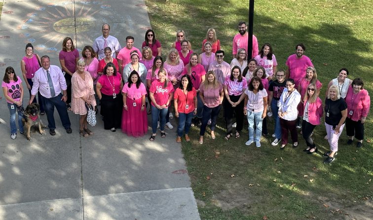 big group of middle school staff members together on the sidewalk looking upward and wearing a lot of pink for breast cancer awareness