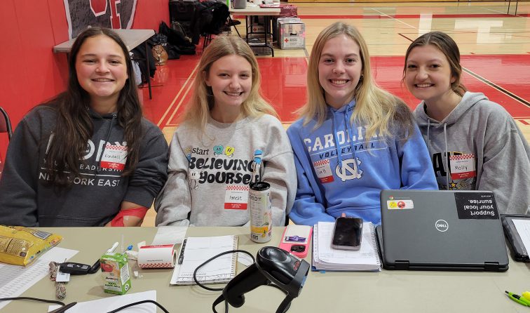 four student chairpersons sit at hte check-in table for the high school's blood drive in the gym