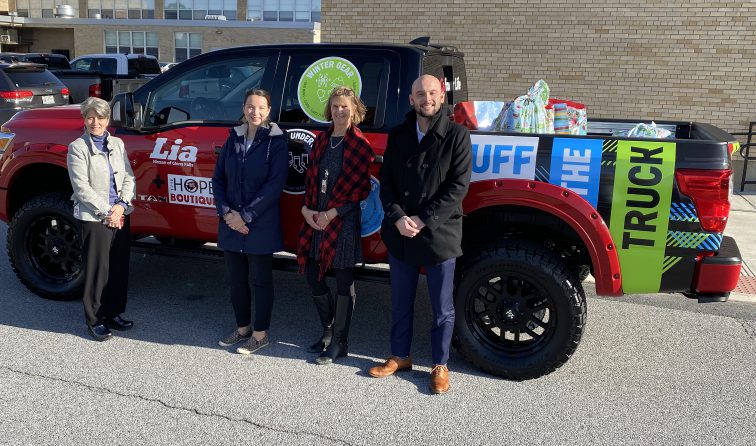 four people smiling in front of a bright red pickup truck from Lia Auto Group that has several huge bags of donated gifts in the back of it