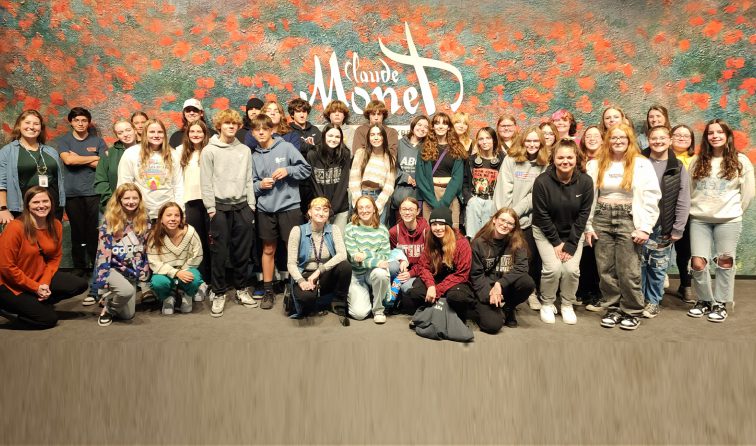 large group of student-artists in front of the Claude Monet immersive experience sign