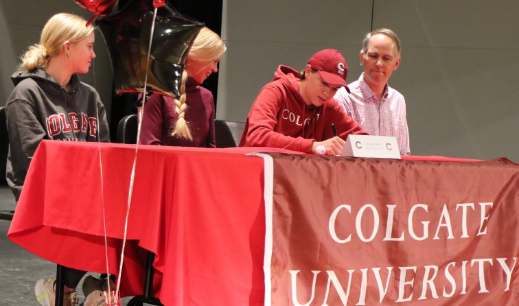 student-athlete and his parents and sister sitting at a red tablecloth-draped table with a Colgate University flag, signing his letter of intent