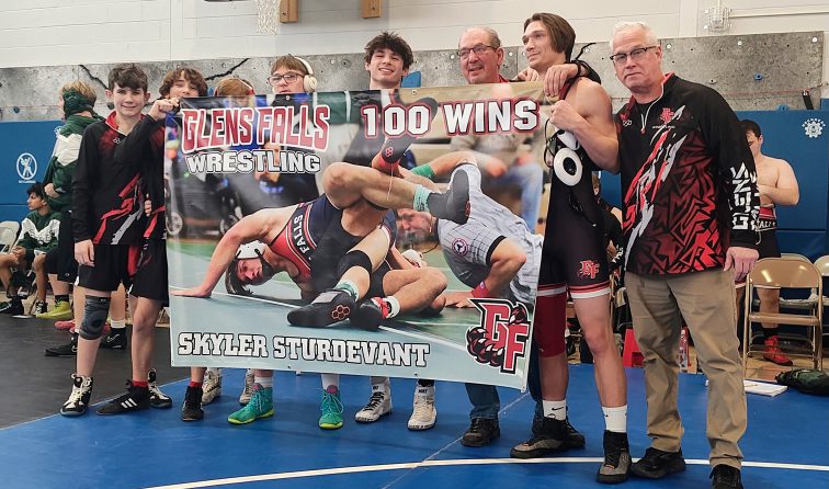 group of high school wrestlers and coaches holding a banner congratulating teammate on 100 wins