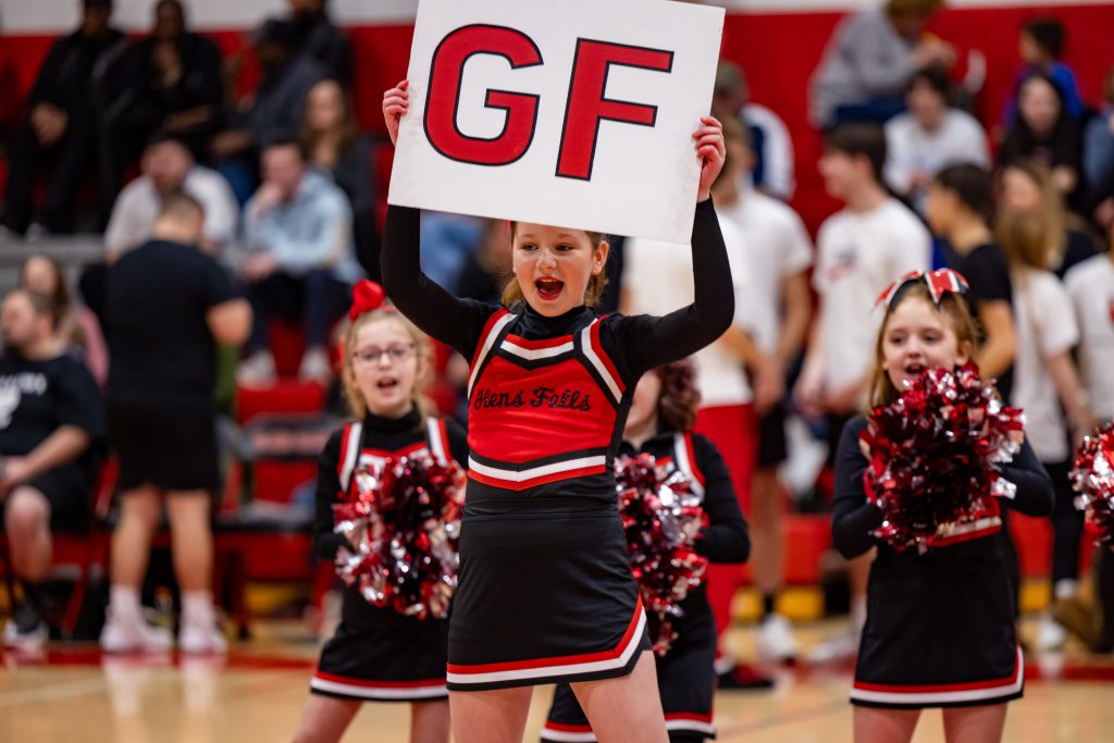 A spunky Glens Falls PAL cheerleader holds up a sign reading "GF" while several other cheerleaders clap their pom-poms in the background