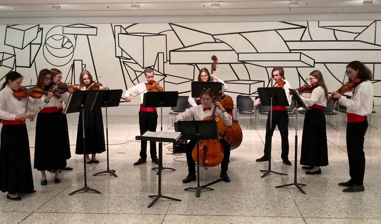 group of chamber orchestra students playing their instruments in front of an artistic mural