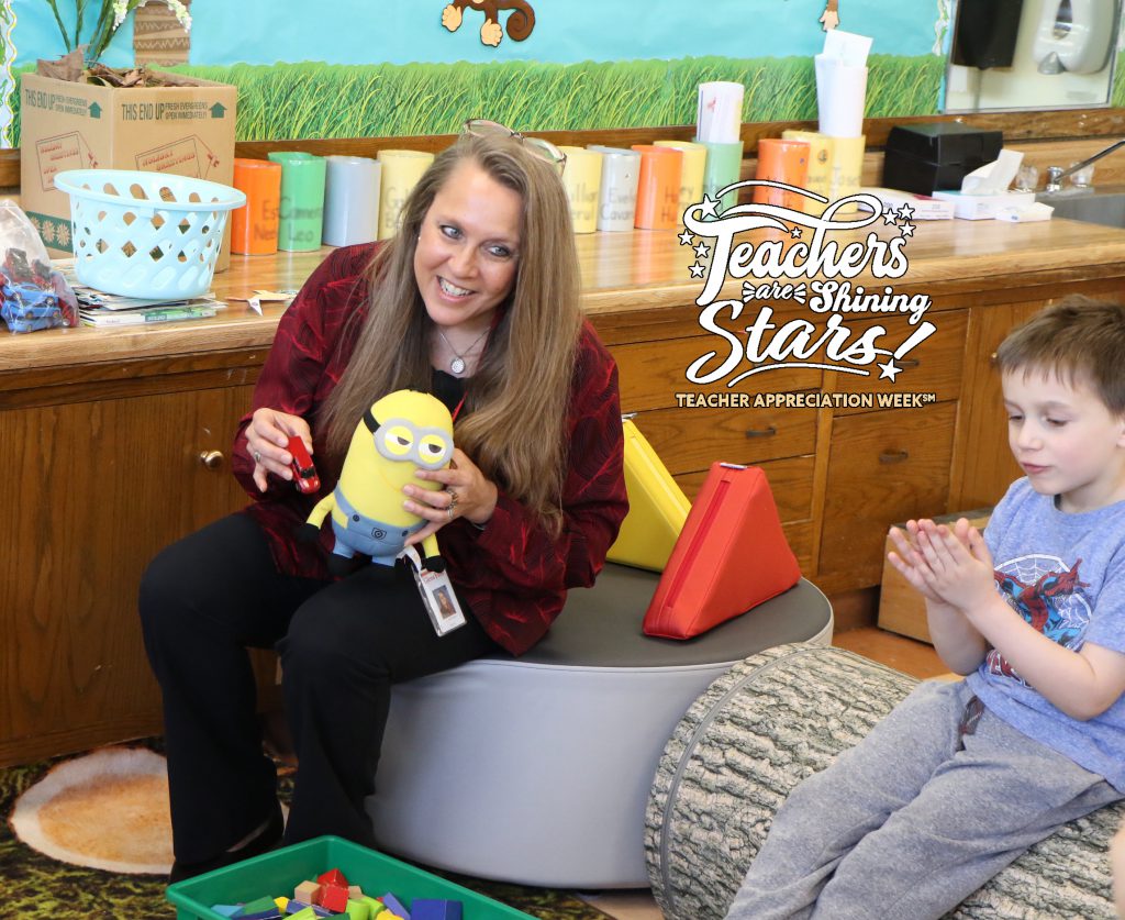 Kindergarten teacher in bright classroom laughing with students during a lesson with a stuffed animal